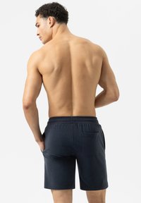 Marineblauwe shorts van katoen, met een elastische tailleband en zijzakken, gezien vanuit de rug op een model met een bloot bovenlijf.
