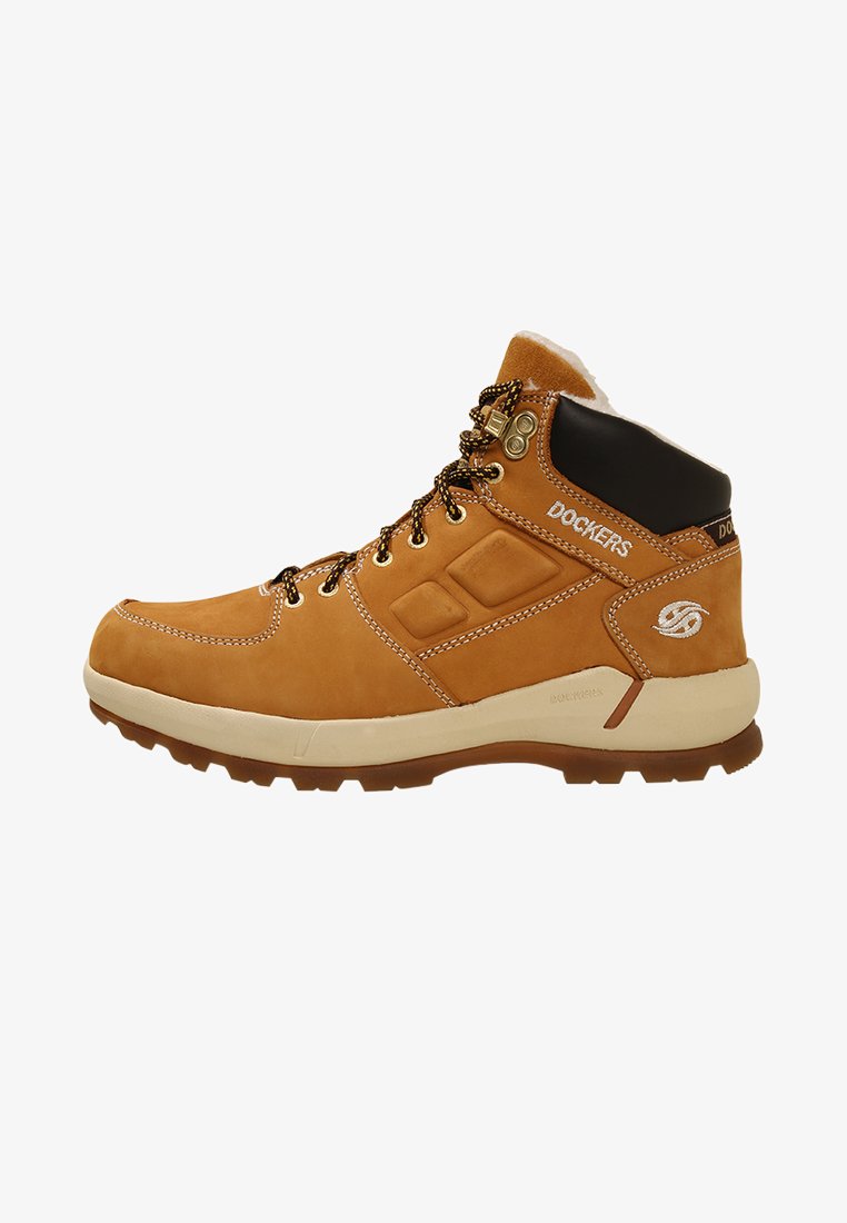Botte de randonnée en cuir tan avec un col rembourré noir, des œillets en metal et des coutures contrastantes. Dispose d'une semelle en caoutchouc texturée pour une meilleure adhérence.
