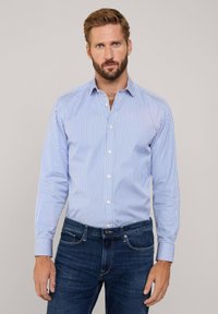 Camicia a righe blu e bianche con bottoni, maniche lunghe e colletto, abbinata a jeans in denim scuro. Tessuto liscio, vestibilità standard.