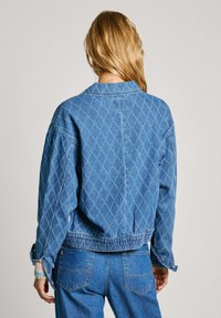 Giacca di jeans di colore azzurro chiaro con motivo a diamante, vita elasticizzata e spalle scese. Caratterizzata da maniche lunghe con polsini a bottone.