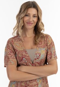 Kobberød og guld paisley mønster bluse med korte ærmer og en dyb V-hals, lavet af blødt stof. Bunden er i en varm rød tone.