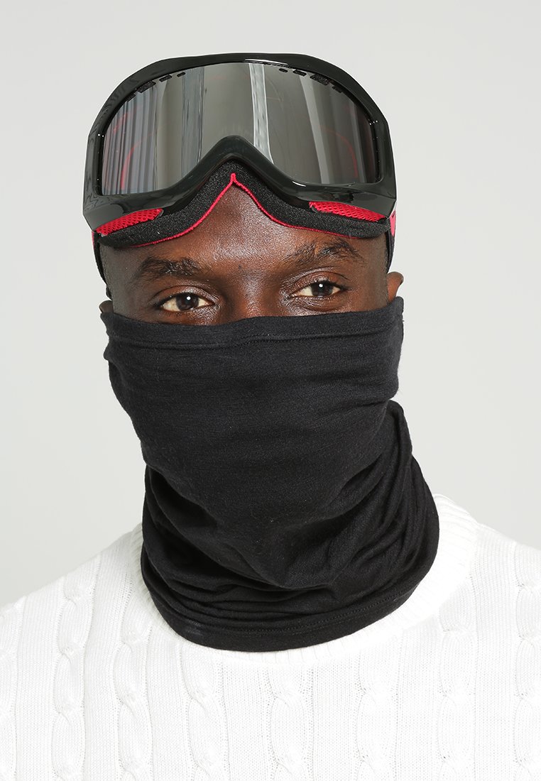 Gaiter nera indossato con occhiali da sci caratterizzati da una montatura nera lucida e dettagli rossi, su un maglione bianco lavorato a maglia a trecce.