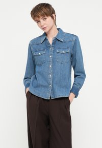 Jasnoniebieska koszula dżinsowa z długim rękawem, zapinana na guziki z przodu, z dwiema kieszeniami na piersi i klasycznym kołnierzykiem. Miękka tekstura i luźny krój.