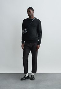 Μαύρη φλις ζακέτα με ραμμένες μανσέτες, σκούρες τζιν παντελόνες, λευκές κάλτσες και μαύρες μοκασίνες. Μικρή μαύρη τσάντα χιαστί με λεπτομέρεια από μέταλλο.