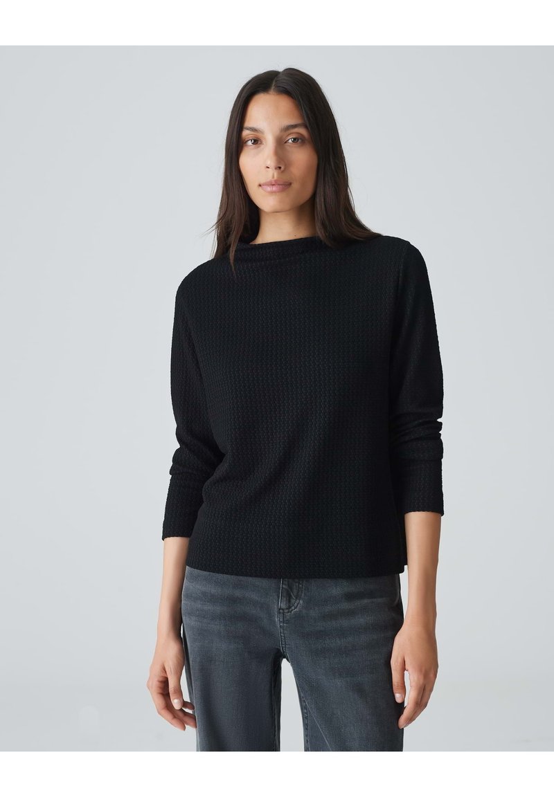 Schwarzer strukturierter Pullover mit Rundhalsausschnitt und langen Ärmeln, kombiniert mit dunkelgrauen Jeans. Der Stoff weist ein dezentes Muster auf.