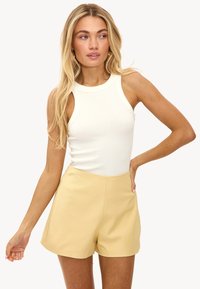 Débardeur blanc à côtes avec un décolleté arrondi associé à un short jaune taille haute, présentant un tissu lisse et une silhouette ajustée.