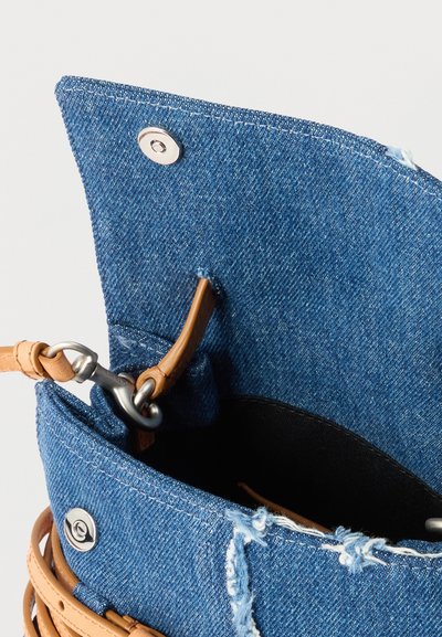 Τσάντα από τζιν με ξεφτισμένες άκρες, λουρί από ταμπά δέρμα και κούμπωμα με ασημένιο κουμπί, που δείχνει το ανοιχτό επάνω μέρος και το μεταλλικό κούμπωμα σύνδεσης.