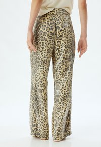 Leopardscratch brede pantalon in beige en zwart, met een gladde textuur en een hoge taille. Achteraan zichtbaar een vloeiende pasvorm en stijl.