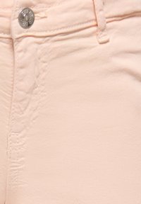 Light pink denim fabric with visible stitching, a metal button at the waistband, and a smooth texture. Features a classic five-pocket design.