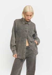 Grijze denim shirt met knoopsluiting, lange mouwen en twee voorzakken, gecombineerd met bijpassende grijze wijde broek.