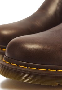 Gros plan de bottes en cuir marron foncé avec des coutures jaunes et des semelles épaisses en caoutchouc translucide.