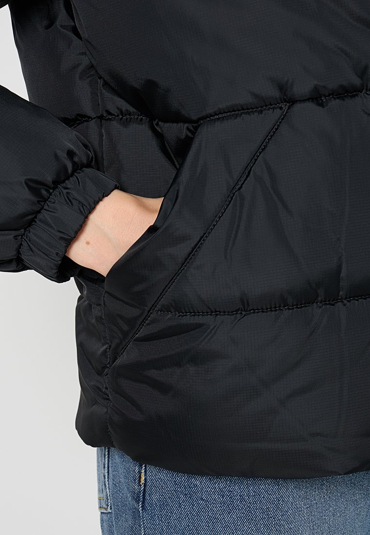 Schwarze Daunenjacke mit glatter, glänzender Außenoberfläche. Verfügt über elastische Bündchen und eine Seitentasche. Der Stoff wirkt leicht und komprimierbar.