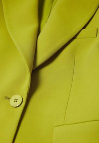 Blazer verde lima a medida con una textura suave, solapa con muesca, cierre de un botón y detalles de bolsillo lateral.