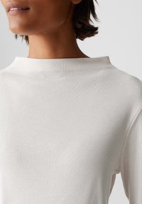 Weißes, geripptes Langarmoberteil mit hohem Halsausschnitt und lässiger Passform, das eine glatte Textur und ein minimalistisches Design aufweist.