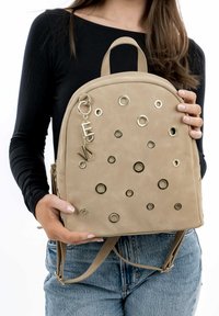 Zaino in ecopelle color cuoio con occhielli dorati, accenti circolari e decorativi. Dotato di doppie spalline e manico superiore per il trasporto.
