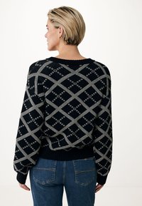 Svart stickad tröja med vitt diamantmönster, med rund halsringning, ribbade muddar och en avslappnad passform, i kombination med blå jeans.