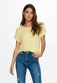 T-shirt giallo a maniche corte realizzato in tessuto morbido, abbinato a jeans blu strappati a vita alta. Taglio semplice e rilassato con maniche arrotolate.