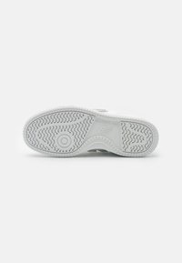 Semelle de chaussure de sport blanche en caoutchouc texturé, avec un motif circulaire et un détail de marque. Offre une adhérence robuste et une surface lisse pour une traction optimale.