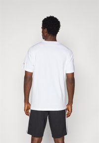 Hvit bomulls T-skjorte med korte ermer, rund hals og løs passform, kombinert med svarte shorts med hvite sidestriper.