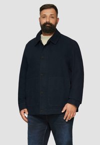Granatowa kurtka wykonana z bawełny z zapięciem na guziki, spiczastym kołnierzem i dwoma dolnymi kieszeniami naszytymi. Ma luźny krój i długie rękawy.