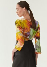 Multikleurige blouse met een bloemmotief, vloeiend materiaal, driekwart mouwen en een ronde halslijn. Gecombineerd met een donkere, aansluitende rok.