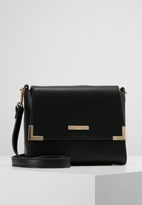Černá syntetická kožená crossbody taška se zlatými kovovými prvky, obdélníkový tvar, klopový uzávěr a nastavitelný popruh. Ozdobena logovým štítkem.