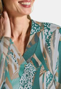 Multicolore blouse met een V-hals, met een mix van groene, beige en witte patronen in strepen en abstracte vormen. Getextureerde stof.