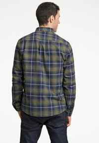Camisa de cuadro verde y marino con mangas largas, puños abotonados y un cuello estándar, que cuenta con un dobladillo curvado y sutiles detalles en blanco.