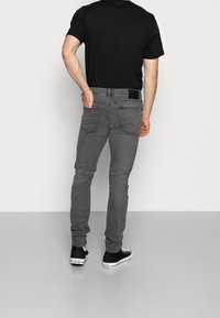 Szare dżinsy o slim fit, z standardowymi kieszeniami i czarną metką w pasie. W połączeniu z czarnymi trampkami.