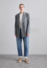 Blazer grigio oversize con due bottoni, abbinato a una t-shirt bianca e jeans cropped azzurri chiari. Sneakers marroni con dettagli crema.