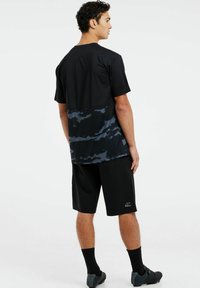 Čierne atletické tričko s priedušným tmavomodrým maskáčovým vzorom na dolnej polovici, spárované s čiernymi šortkami. Materiál vyzerá ľahko.