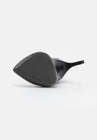 Escarpin noir à bout pointu posé sur le côté, montrant la semelle avec la marque Calvin Klein sur un fond blanc.