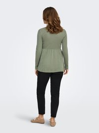 Long-sleeve, light green, textured top with a peplum design, paired with black slim-fit pants and beige slip-on shoes.