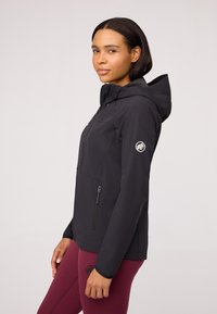 Black hooded jacket with zipper pockets, made of soft material, featuring a subtle logo on the sleeve and a fitted design.