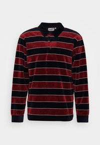 Polo met lange mouwen met rood en zwarte horizontale fluwelen strepen, zwarte kraag en knoopsluiting op een witte achtergrond.