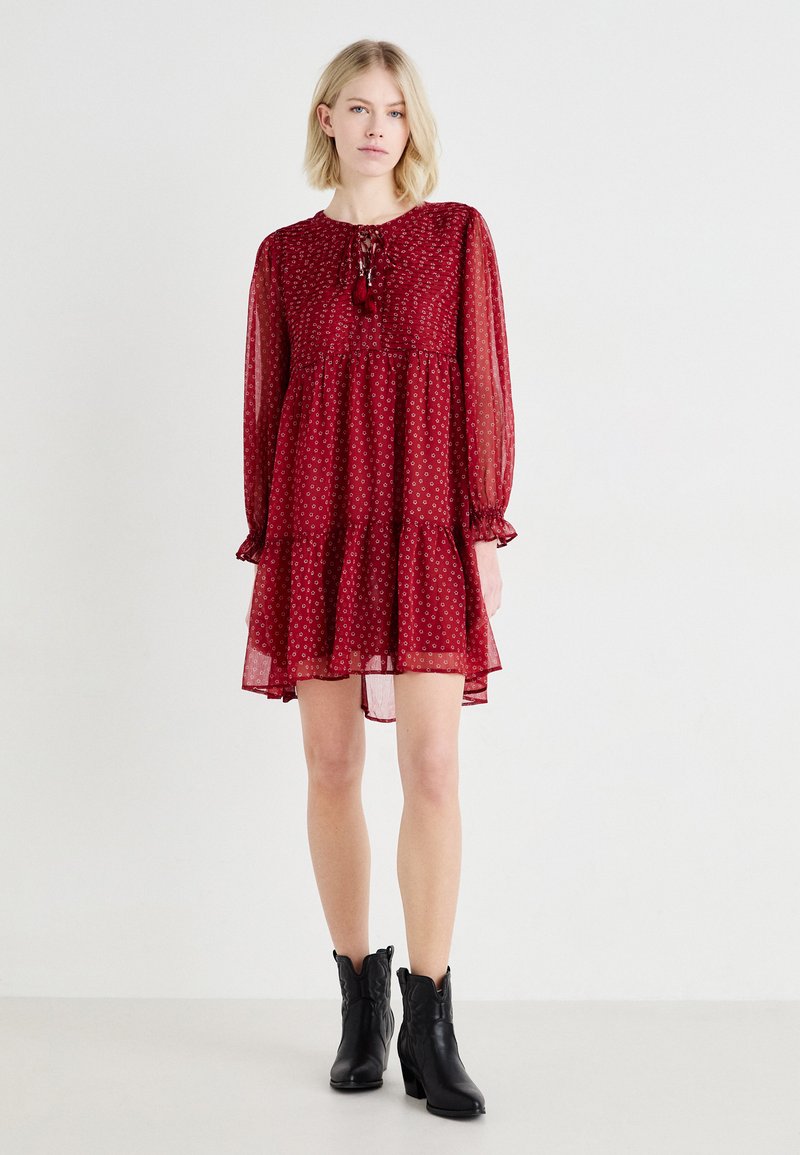 Rochie roșie din material translucid, cu mâneci lungi, talie plisată și tiv ondulat. Prezintă un model floral și un decolteu cu panglică. Asortată cu botine negre până la gleznă.