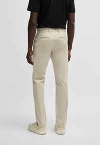 Beige chinos lavet af fleksibelt stof, med lige ben design, diskrete baglommer, og kombineret med lyse sneakers.