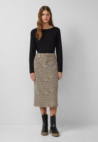Haut à manches longues noir associé à une jupe midi en imprimé léopard beige. Le mannequin porte des bottes noires épaisses avec une semelle texturée.