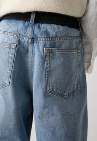 Jeans de mezclilla azul claro con un corte relajado, que presentan una cinturilla elástica negra y dos bolsillos traseros con costuras en contraste.