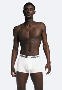 Vita bomullsboxer med en svart "ALLSAINTS" midja, som visar en åtsittande design och en slät textur. Modellen står mot en neutral bakgrund.