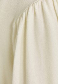 Gros plan sur un tissu doux de couleur crème, rassemblé avec une texture et des plis visibles.