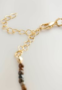 Goldfarbener Kettenarmreif mit ovalen Gliedern, ausgestattet mit einem Karabinerverschluss; am einen Ende sind Perlen in verschiedenen Erdtönen befestigt.