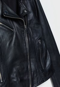 Černá kožená motocyklová bunda se stříbrnými zipovými uzávěry, šikmými postranními kapsami a klopovým límcem; texturovaný povrch, těsně padnoucí design.
