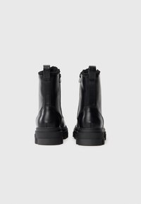 Sorte lær ankle boots med et teksturert bakpanel, som har en trekkflik, solid gummisåle og glidelås på siden.
