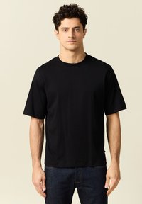 T-shirt nero a maniche corte realizzato in un materiale morbido, con un classico scollo rotondo e una vestibilità ampia, abbinato a jeans scuri.