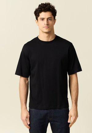 Zwarte t-shirt met korte mouwen van een zacht materiaal, met een klassieke ronde hals en een losse pasvorm, gecombineerd met donkere spijkerbroek.