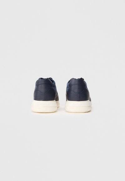 Baskets en cuir bleu marine avec une texture lisse, une conception à l'arrière arrondi et des semelles en caoutchouc blanches. Présente un logo discret au niveau du talon.
