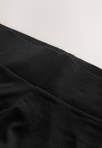 Gros plan d'un tissu noir plié avec une texture lisse sur un fond clair uni.
