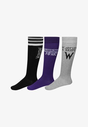 Trois paires de chaussettes montantes : noires avec des rayures blanches et du texte, violettes avec "AVERTISSEMENT TOXIQUE", et grises avec des éléments de design "SANS CŒUR & HEUREUX".