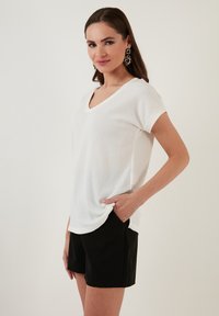 Top bianco a maniche corte e scollo a V con un tessuto testurizzato, abbinato a pantaloni corti neri. Il top ha una vestibilità rilassata e tasche laterali.